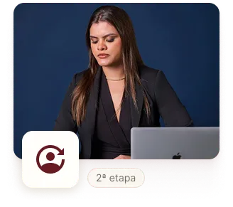 ="Mulher de cabelos castanhos lisos, vestindo blazer preto, sentada em frente a um notebook Apple sobre uma mesa. Ela está concentrada, com expressão séria, contra um fundo azul escuro. No canto inferior esquerdo há um ícone circular com setas e a legenda '2ª etapa'.